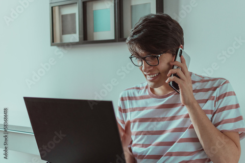 hombre joven hablando por celular en frente del laptop 
