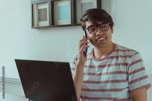 hombre joven hablando por celular en frente del laptop 