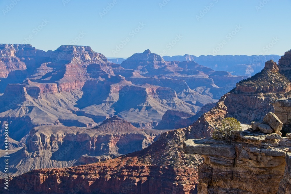 Fototapeta premium Bright desert sunlight shines down on the Grand Canyon, casting shadows on every crease and layer of the eroded canyon carved over many years by the Colorado River thousands of feet below