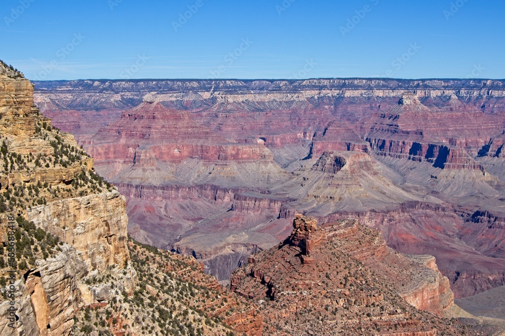 Bright desert sunlight shines down on the Grand Canyon, casting shadows on every crease and layer of the eroded canyon carved over many years by the Colorado River thousands of feet below