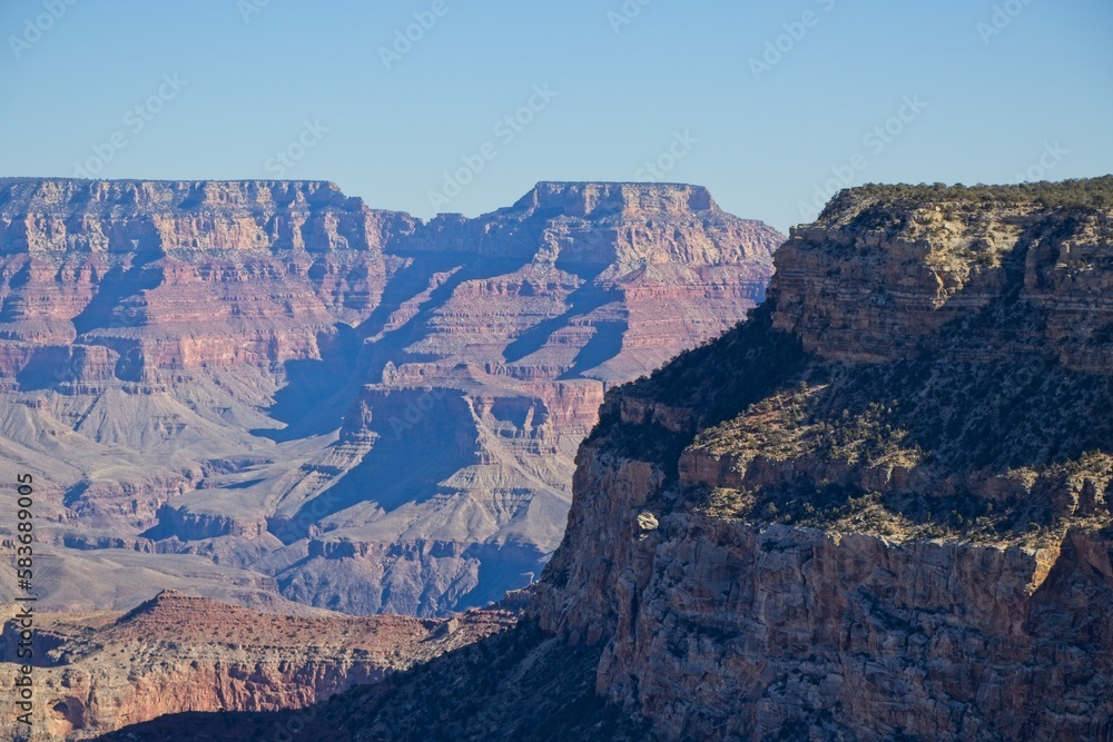 Bright desert sunlight shines down on the Grand Canyon, casting shadows on every crease and layer of the eroded canyon carved over many years by the Colorado River thousands of feet below