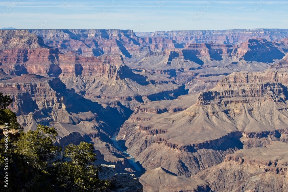 Bright desert sunlight shines down on the Grand Canyon, casting shadows on every crease and layer of the eroded canyon carved over many years by the Colorado River thousands of feet below Bright desert sunlight shines down on the Grand Canyon, casting shadows on every crease and layer of the eroded canyon carved over many years by the Colorado River thousands of feet below