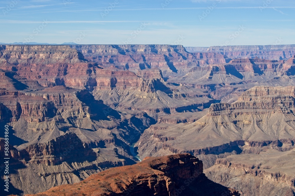 Bright desert sunlight shines down on the Grand Canyon, casting shadows on every crease and layer of the eroded canyon carved over many years by the Colorado River thousands of feet below