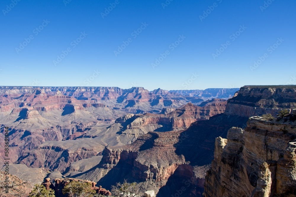 Bright desert sunlight shines down on the Grand Canyon, casting shadows on every crease and layer of the eroded canyon carved over many years by the Colorado River thousands of feet below