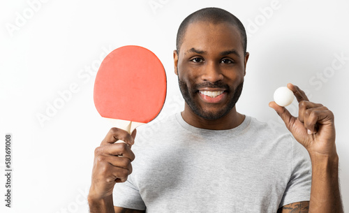 A bald, dark-skinned adult man posing on a white background with a ping.pong racket and a ball. Concept of ping-pong player. photo