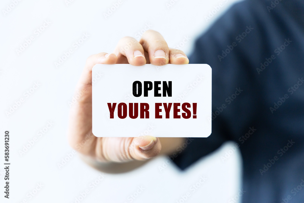 Open your eyes text on blank business card being held by a woman's hand with blurred background. Business concept about looking for new things. Open your eyes text on blank business card being held by a woman's hand with blurred background. Business concept about looking for new things.