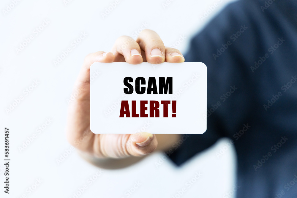 Scam alert text on blank business card being held by a woman's hand with blurred background. Business concept about scam. Scam alert text on blank business card being held by a woman's hand with blurred background. Business concept about scam.
