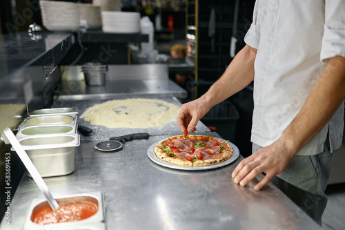 Pizzaiolo making pizza at kitchen with closeup focus on hand