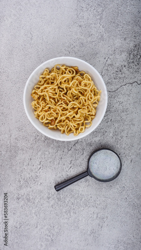 instant noodles with magnifying glass in the bowl on cement texture background