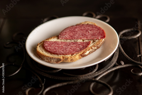 Bread with salami on a white plate on a dark background. Simple sandwich.