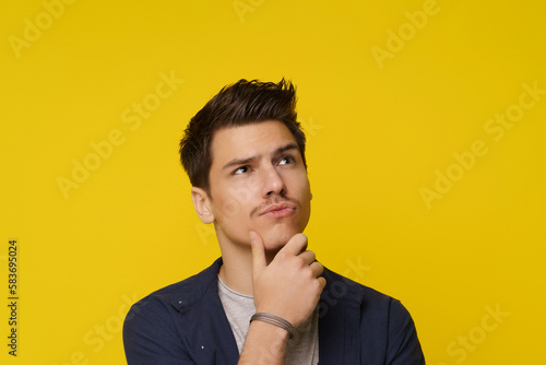 Close up of young man on yellow background, with facial expression conveying confusion and uncertainty, as he thinks and has doubt. Complex and emotional nature of decision-making and contemplation