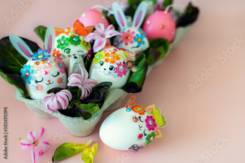 Easter eggs decorated with hare and cat muzzles in a patch with leaves and flowers on a pink background.