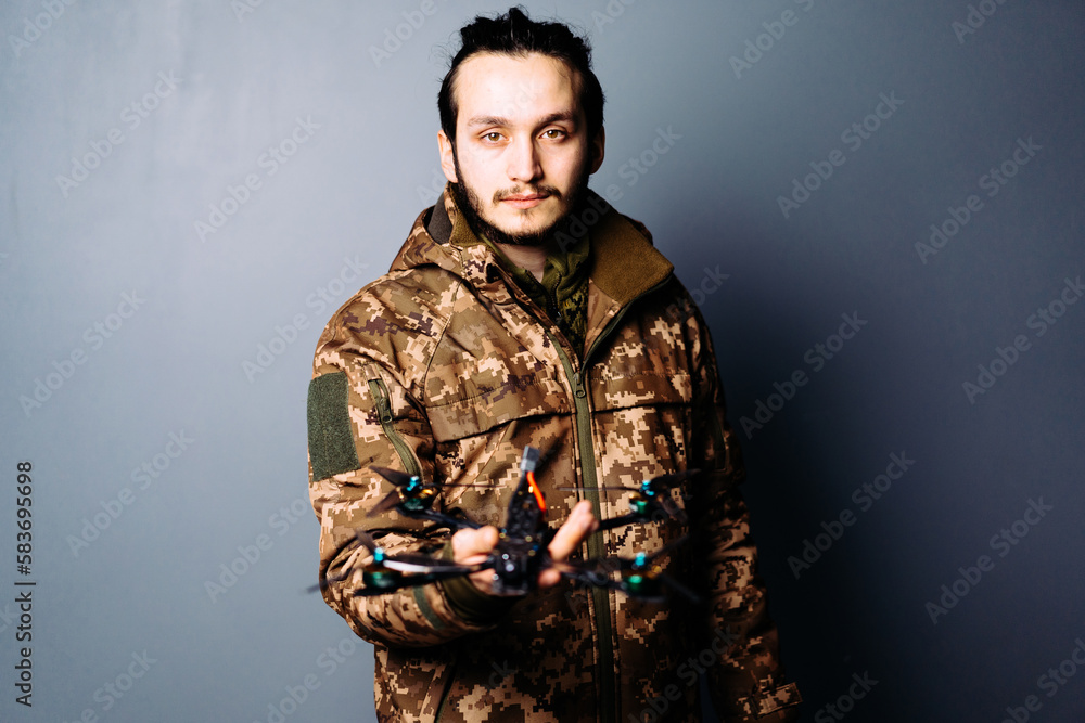 Soldier in military camouflage uniform holding fpv racing kamikaze drone bomber on blue background