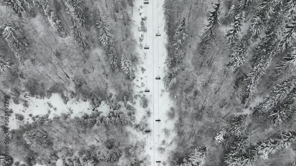 Aerial view over snowy mountain winter forest with chair lift at ski resort. Ski lift cable car top down drone shot. Winter landscape scene with snow covered trees. Outdoor tourism skiing snowboarding Aerial view over snowy mountain winter forest with chair lift at ski resort. Ski lift cable car top down drone shot. Winter landscape scene with snow covered trees. Outdoor tourism skiing snowboarding