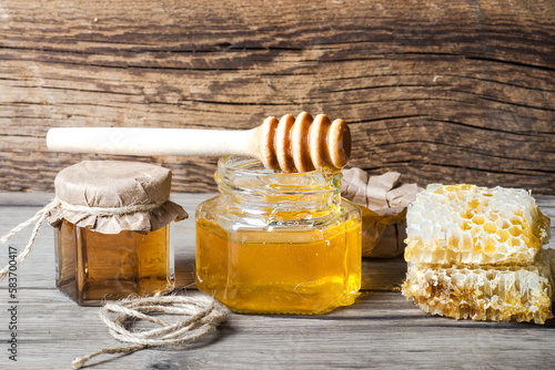 Two jars of honey, a dipper and honeycomb on gray wooden table. Space for text.