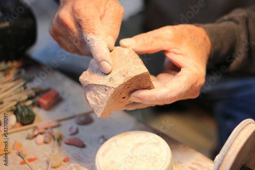 Hands of elderly craftsman man working in a workshop polishing opal stones and minerals to form precious jewelry 