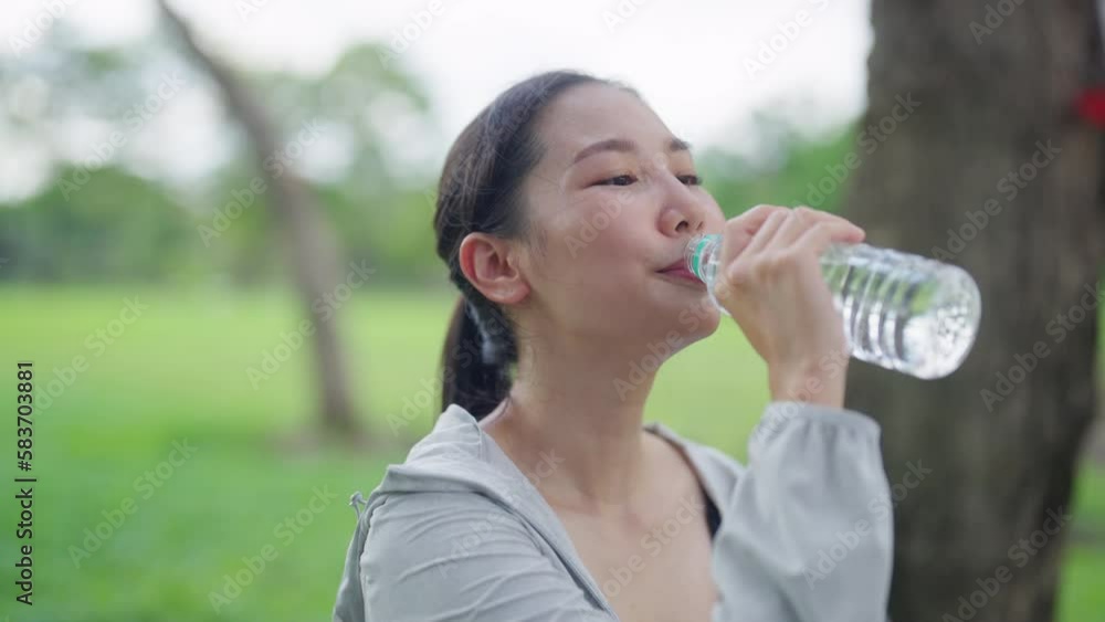 Asian woman in sportswear drinking water from a bottle during jogging exercise at public park in the morning. Healthy girl athlete enjoy outdoor lifestyle sport training workout running in the city. Asian woman in sportswear drinking water from a bottle during jogging exercise at public park in the morning. Healthy girl athlete enjoy outdoor lifestyle sport training workout running in the city.