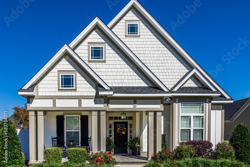 The front view of a cottage craftsman style white house with a triple pitched roof with a sidewalk, landscaping and curb appeal