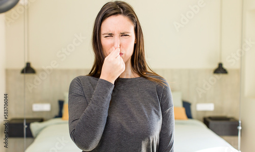young adult pretty woman feeling disgusted, holding nose to avoid smelling a foul and unpleasant stench