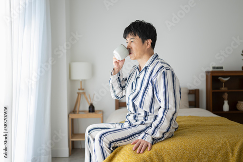 朝、ベッドでコーヒーを飲む50代男性