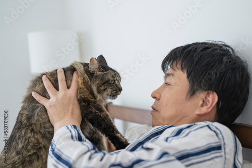 目が覚めてベッドで猫と戯れる50代男性