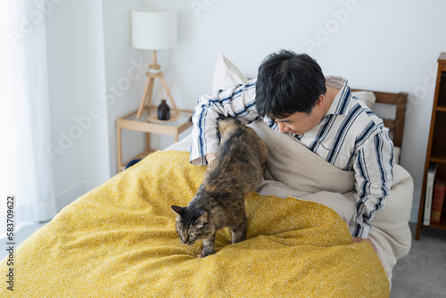 目が覚めてベッドで猫と戯れる50代男性