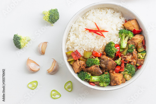 Stir fried chicken and broccoli bell pepper has rice in bowl on white wood table.