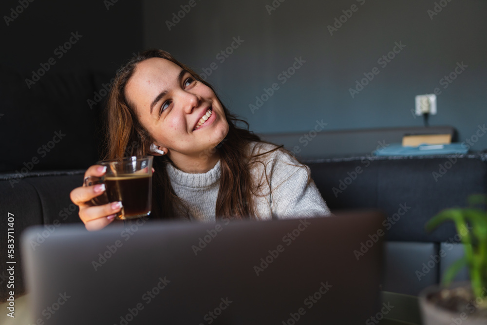 A young girl sitting at home while using laptop to study or do business while drinking coffee and using mobile phone A young girl sitting at home while using laptop to study or do business while drinking coffee and using mobile phone