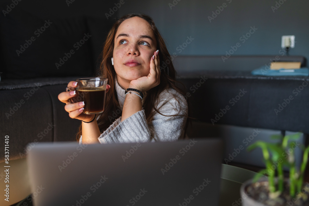 A young girl sitting at home while using laptop to study or do business while drinking coffee and using mobile phone A young girl sitting at home while using laptop to study or do business while drinking coffee and using mobile phone