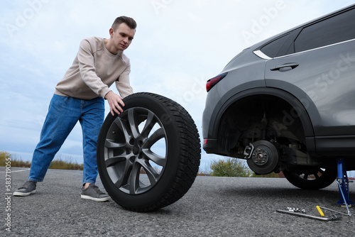 Young man changing tire of car on roadside © New Africa