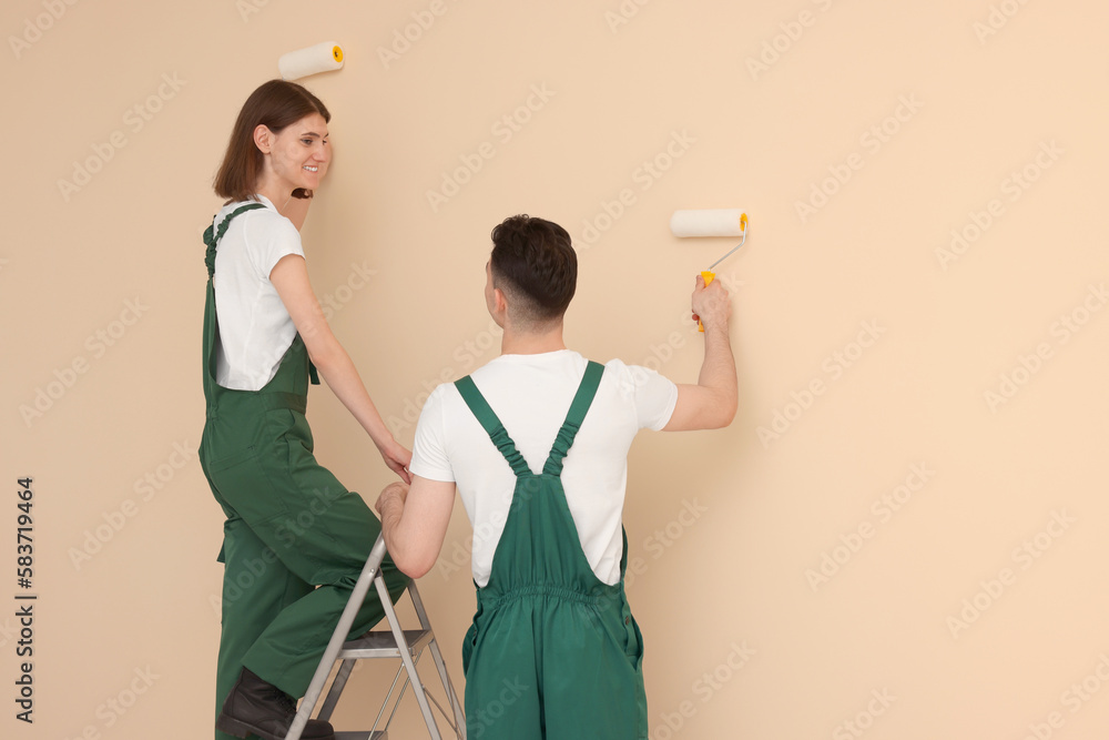 Young workers painting wall with rollers indoors. Room renovation