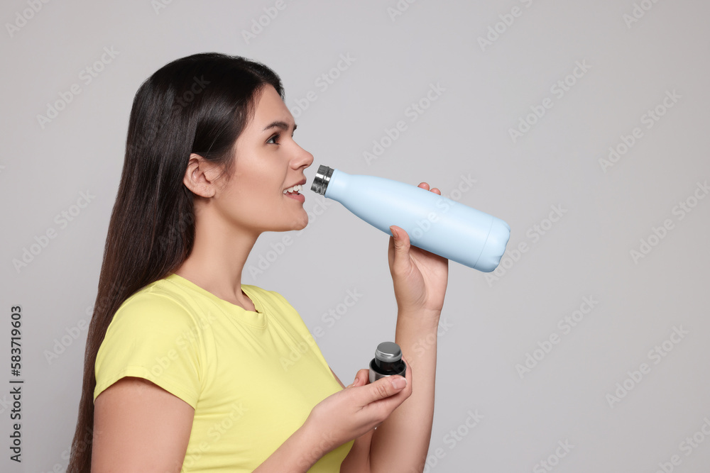 Young woman drinking from thermo bottle on light grey background. Space for text Young woman drinking from thermo bottle on light grey background. Space for text