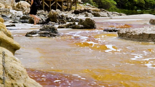 Beachgoers walk over tannin-rich lagoon water running out to ocean over beach photo