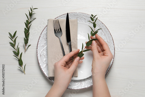 Φωτογραφία Woman adjusting stylish table setting with eucalyptus leaves on white wooden bac