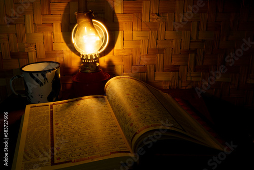 Holy Quran on the wooden table with vintage traditional kerosene lamp and woven bamboo as background.
