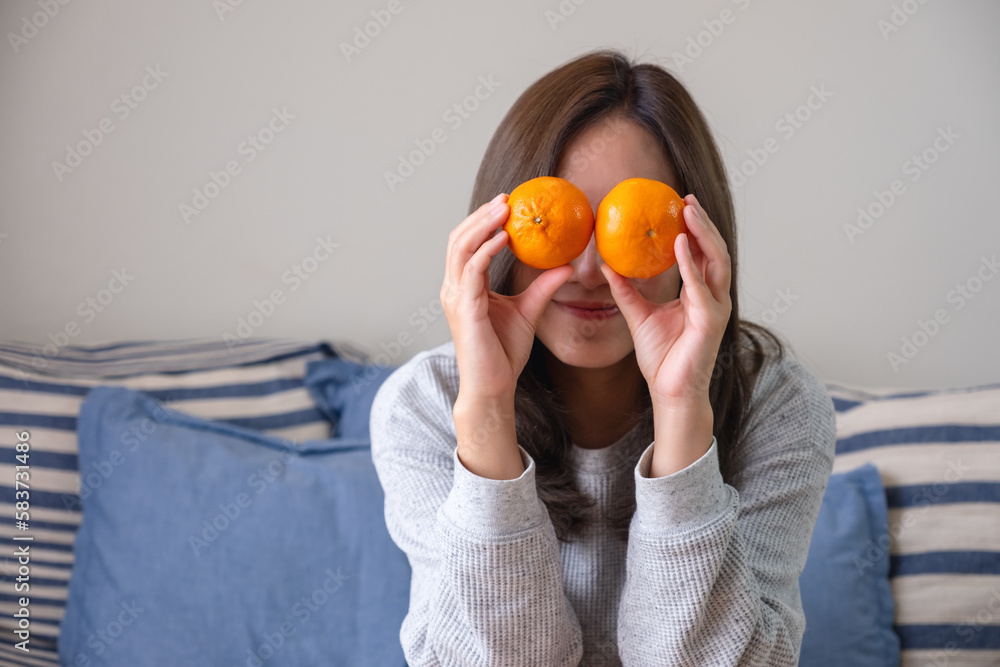 A young woman holding and covering eyes with an oranges A young woman holding and covering eyes with an oranges