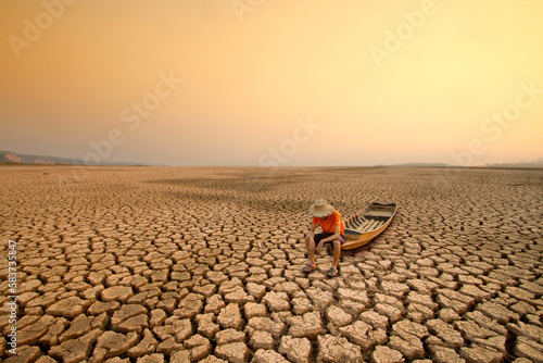 Young man sit on wooden boat with landscape of dry lake or river metaphor climate change, Drought impact.