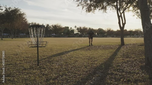 Disc Golfer Makes a Nonchalant In Line Putt 25 Feet from the Disc Golf Basket photo