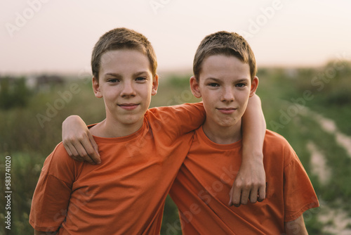Tableau sur toile Funny twin brother boys in orange t-shirt playing outdoors on field at sunset
