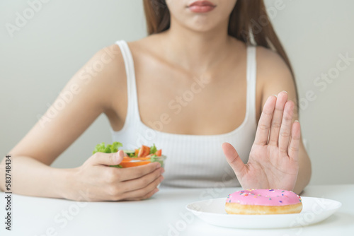 Diet, Dieting asian young woman, girl hand push out, deny sweet donut on plate, dish and choose to eat green salad vegetables in bowl on table, food good healthy, health person, female weight loss.