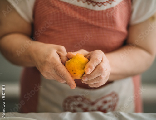 Lifestyle, education. An elderly woman with down syndrome is studying in the kitchen peel the tangerine herrself