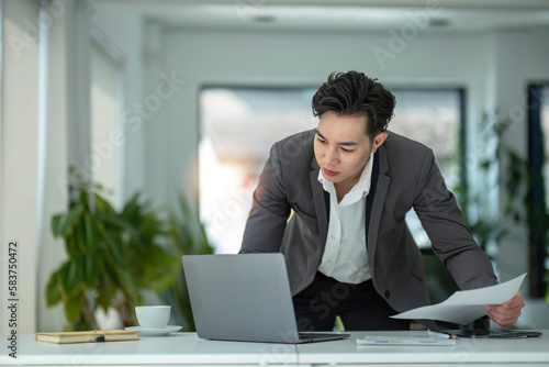 Happy satisfied millennial man using laptop at office workplace, working from home, reading message with good news, thinking, looking at screen, watching online webinar, training, making payment