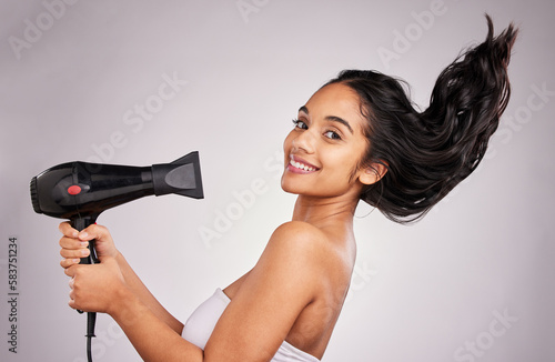 Obraz na plátne Portrait, blow dry and hair with a model woman in studio on a gray background holding an appliance