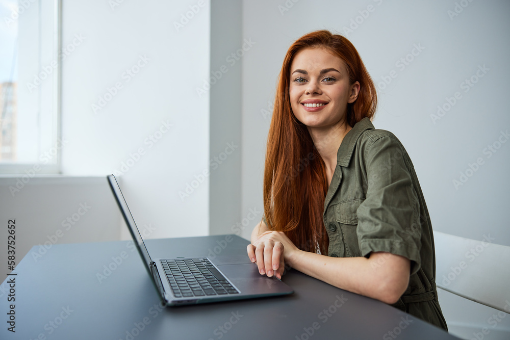 portrait of a cute, smiling red-haired woman sitting at a laptop with her hands folded on the table and looking at the camera portrait of a cute, smiling red-haired woman sitting at a laptop with her hands folded on the table and looking at the camera