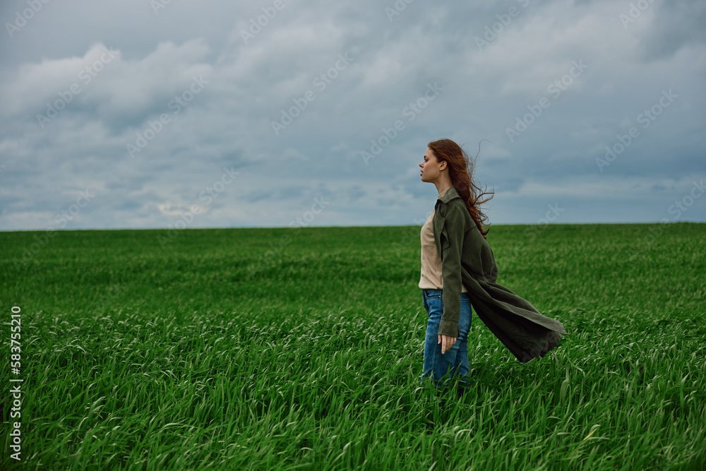 a beautiful woman stands in a green field in a raincoat and looks into the distance. Strong wind, flying hair, harmony with nature a beautiful woman stands in a green field in a raincoat and looks into the distance. Strong wind, flying hair, harmony with nature