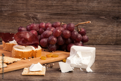 Ham, crackers, grape and white cheese on wooden background in studio photo