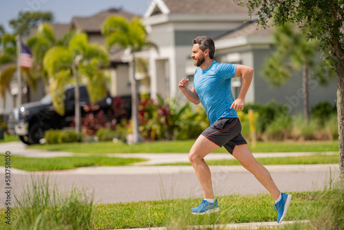 Man running on street in neighborhood. Handsome athlete running in the street. Full length shot of man in sportswear running, urban training.