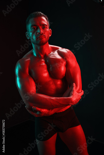 Fashion portrait of an athletic trim attractive man. Manly naked torso in his underpants. Colored flash of studio neon light. © SHOTPRIME STUDIO