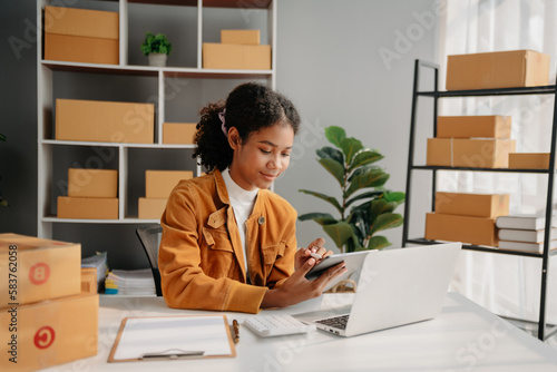 Young African woman prepare parcel box and standing check online orders for deliver to customer on tablet, laptop Shopping Online concept..