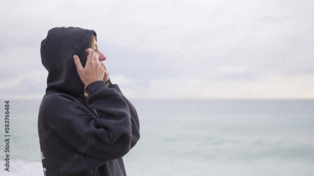 A relaxed woman in a warm sweatshirt with a hood on her head looks out to sea A relaxed woman in a warm sweatshirt with a hood on her head looks out to sea
